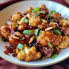 A delicious plate of Spicy Crispy Kung Pao Cauliflower served with roasted peanuts, green onions, and a vibrant stir-fry sauce, garnished with a few dried red chilies.